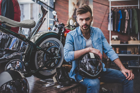 Handsome man in motorcycle shop. Salesman is sitting and looking at camera. Shop assistant on working place.の写真素材