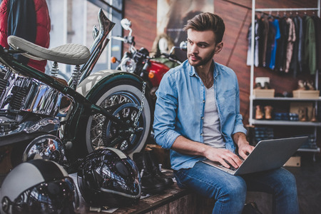 Handsome man in motorcycle shop. Salesman with laptop. Shop assistant on working place.の写真素材