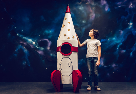 Boy is standing near toy rocket on space background.の写真素材