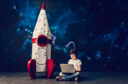 Boy is sitting near toy rocket on space background with laptop.の写真素材