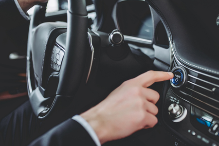 Cropped image of young handsome businessman is sitting in luxury car. Man in suit is driving....