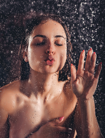 Sexy woman in shower. Attractive young naked woman under water drops isolated on black background.の写真素材