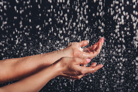 Cropped image of woman in shower. Close-up of woman's hands under the water drops. Hands isolated on black background.の写真素材
