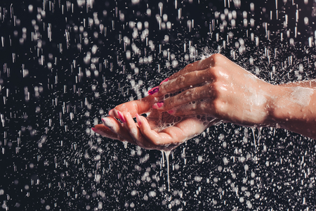 Cropped image of woman in shower. Close-up of woman's hands under the water drops. Hands isolated on black background.の写真素材