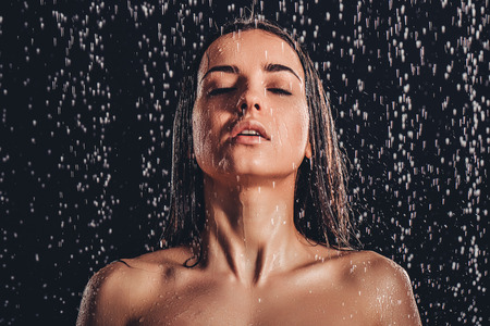 Sexy woman in shower. Attractive young naked woman under water drops isolated on black background.の写真素材