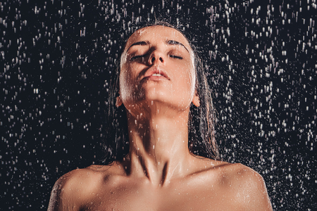 Sexy woman in shower. Attractive young naked woman under water drops isolated on black background.の写真素材
