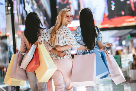 Three attractive young girls are doing shopping with shopping bags in modern mall.の写真素材