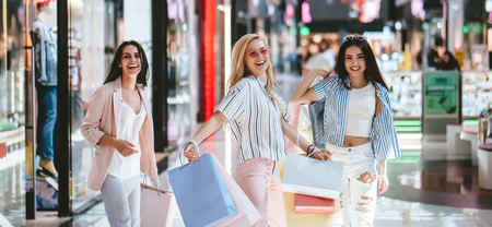 Three attractive young girls are doing shopping with shopping bags in modern mall.の写真素材