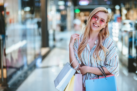 Attractive young happy woman is doing shopping with shopping bags in modern mall.の写真素材