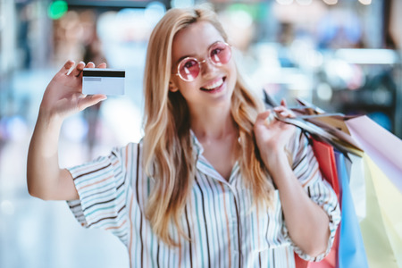 Attractive young happy woman is doing shopping with shopping bags in modern mall. Standing with credit card in hands and smiling.の写真素材