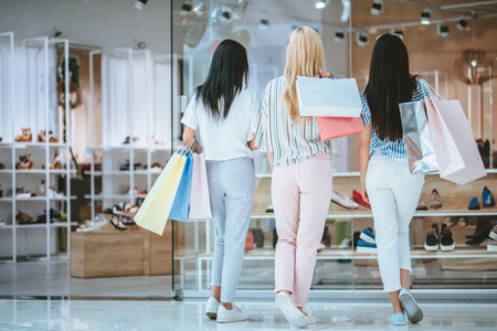 Three attractive young girls are doing shopping with shopping bags in modern mall.の写真素材