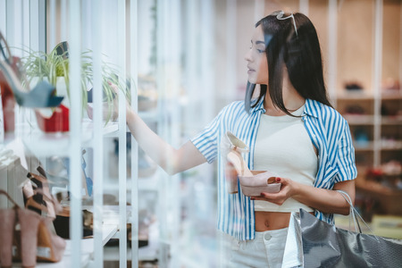 Attractive young girl is doing shopping with shopping bags in shoes store in modern mall.の写真素材