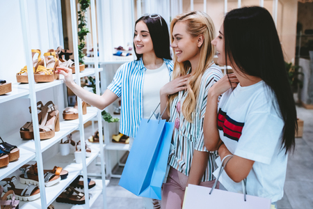 Three attractive young girls are doing shopping with shopping bags in shoes store in in modern mall.の写真素材