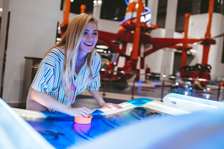 Attractive young woman is having fun in amusement park. Playing table hockey.の写真素材