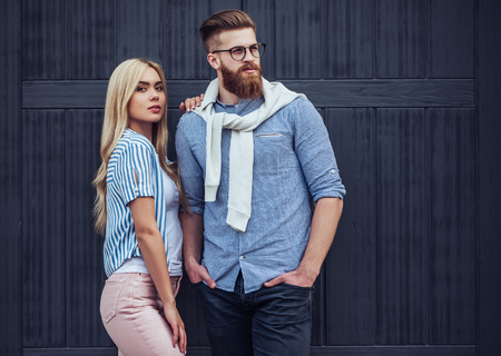 Stylish young couple is spending time together outdoors. Attractive woman and handsome bearded man are posing on black wooden background.の写真素材