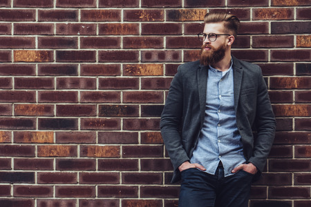 Stylish bearded man is posing on brick background in the city. Young man in eye glasses isolated.の写真素材