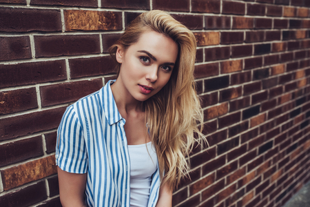 Attractive young woman is posing on brick background in the city. Stylish girl outdoor.の写真素材