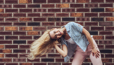 Attractive young woman is posing on brick background in the city. Stylish girl is having fun outdoor.の写真素材