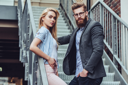 Attractive young happy couple is spending time together outdoors. Attractive woman and handsome bearded man are standing on stairs in the city.の写真素材