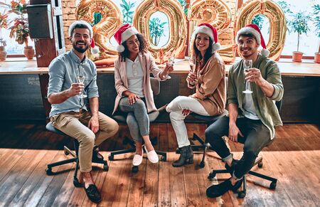 Merry Christmas and Happy New Year 2020!Multiracial young creative people are celebrating holiday in modern office. Group of young business people are drinking champagne in coworking. Successful hipster team of freelancers.の写真素材