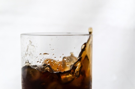 A glass of Cola with ice splashing against a white backgroundの写真素材