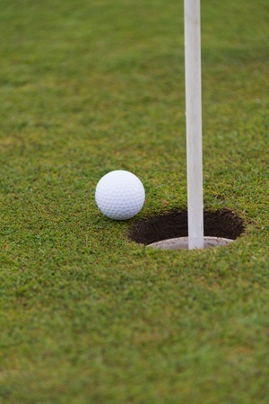 golf ball close to a hole with the flag in placeの写真素材