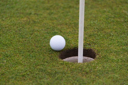golf ball close to a hole with the flag in placeの写真素材