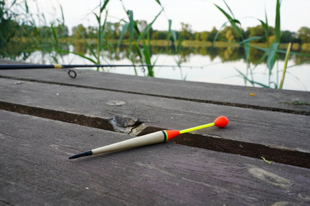 Fishing float, fishing bobber on the wooden pier. Fishing rod and fishing equipment on the jetty at the lake in the forest. Fishing concept.の写真素材