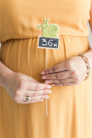 A pregnant woman in a yellow dress is holding a chalk board