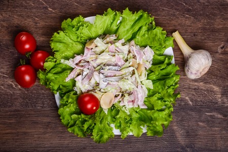 Salad with ham and mushrooms on a lettuce leaf in a white plateの写真素材