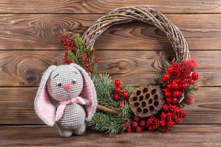 Wreath and hare rabbit. Christmas winter frame on dark wooden background. Red elements Crochet Kraft Toysの写真素材