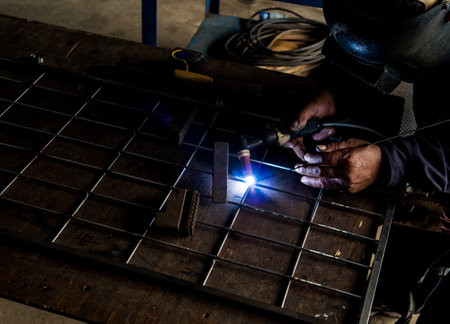 Close up portrait view of professional mask protected welder man in uniform working.