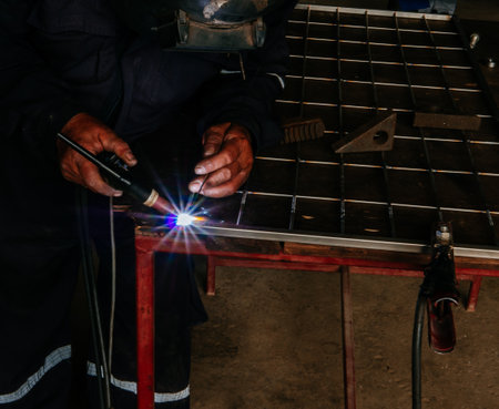 Close up portrait view of professional mask protected welder man in uniform working.