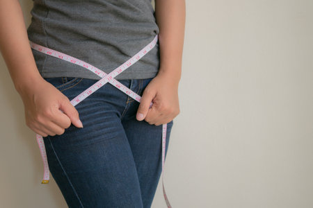 Woman measuring her waist with a tape measure, weight loss concept.