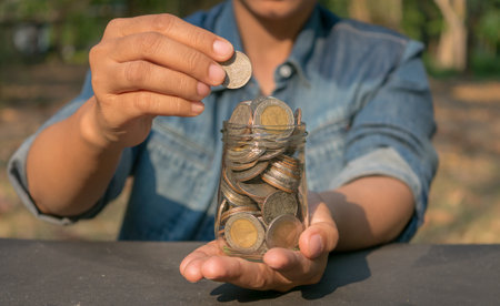 Hands holding coins in a glass jar for save money concept.の写真素材
