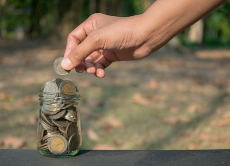 Hand putting coin in the glass jar for save money and account banking concept.