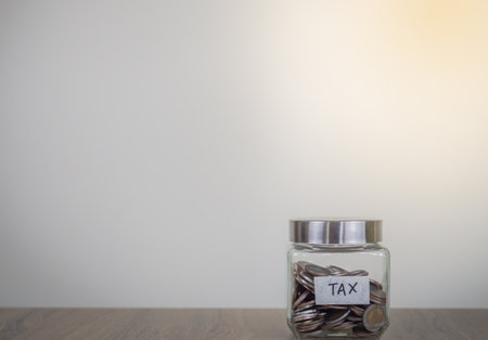 Coins in glass jar with copy space on wooden table and white wall background