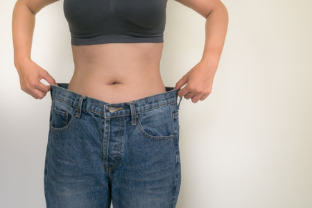 Woman showing how much weight she lost in her old jeans, weight loss conceptの写真素材