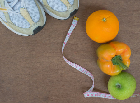 Fitness and healthy lifestyle concept. Sport shoes, apple, tomato and orange on wooden backgroundの写真素材