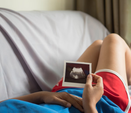 Closeup of pregnant woman holding ultrasound image of her baby in bedroomの写真素材