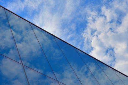Glass curtain wall with blue sky and white cloudsの写真素材