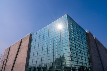 Modern office building with blue glass facade and sun flare on blue skyの写真素材