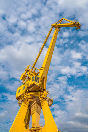 Port cargo crane against blue sky with white clouds. Industrial background.