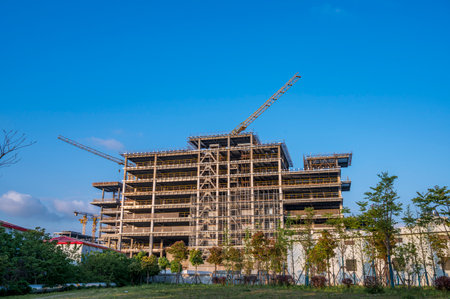 Construction site with cranes and building under construction against blue sky.