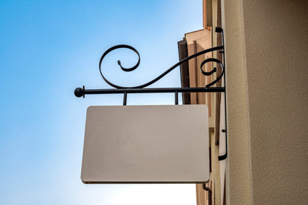 White signboard hanging on the wall of a building, with blue skyの写真素材