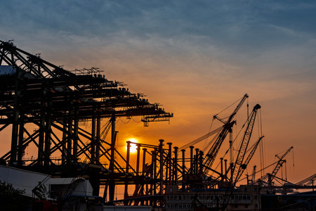 Industrial port with cranes silhouettes on sunset sky background.