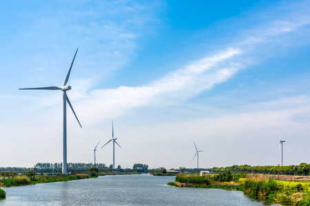 Wind turbines on the bank of a river under a blue cloudy skyの写真素材