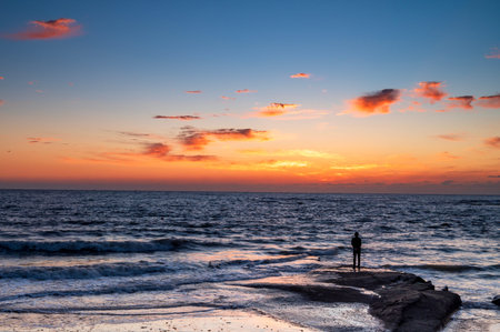 Sunset over the sea, silhouette of a man standing on the rockの写真素材
