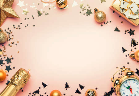 Christmas or New Year composition, frame, pink background with gold Christmas decorations, stars, snowflakes, balls, alarm clock, gift box and bottle of champagne, top viewの写真素材