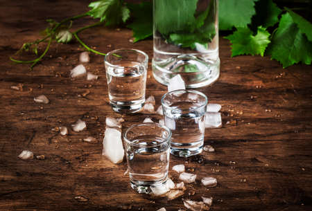 Cold vodka in shot glass, old wooden table, selective focus